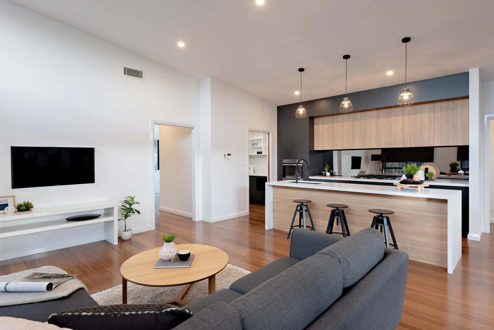 Open plan living and kitchen with island bench, pendant lights and timber floors